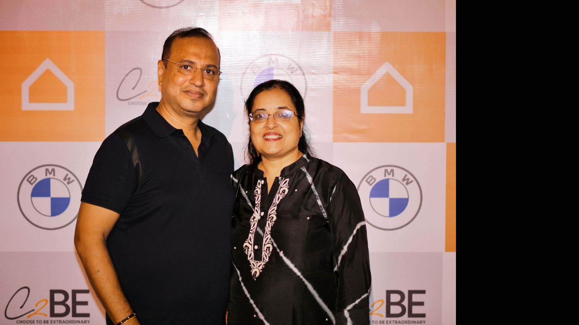 Two guests in front of a branded wall